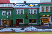 Typical Icelandic green wooden house with snow on the roof in a Reykjavik street and shops with windows with a snow covered sidewalk