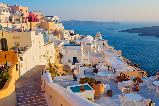 The panoramic view of the old town of Oia or Ia on the island of Santorini, Greece, features, white washed houses, blue dome churches, hotels and traditional windmills. The picturesque landscape captures the beauty of the after-sunrise in la Village, a famous spot on the Greek island of Santorini town. The colorful buildings on the cliffside add to the picturesque atmosphere in Cyclades, Greece. Scenic travel background for romantic vacations and honeymoon holidays.