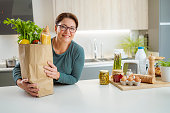 Confident woman holding groceries shopping bag on kitchen counter