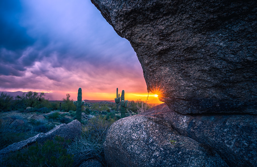 Dramatic sunrise through massive boulder with saguaro cacti in The McDowell Sonoran Preserve