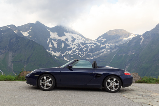 Fusch, Austria - July 25, 2021: Blue roadster Porsche Boxster 986 with mountain panorama at Grossglockner High Alpine Road. The car is a mid-engine two-seater sports car manufactured by Porsche.