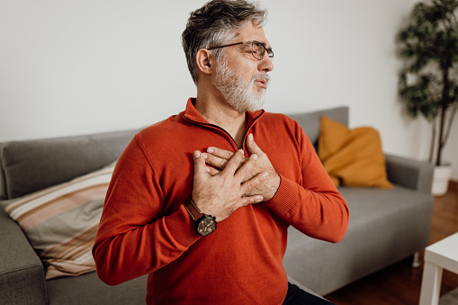 Poor mature Caucasian man feeling strong pain in his chest area while sitting at home all alone