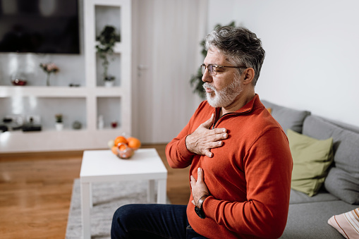 Worried mature Caucasian man feeling strong pain in his chest trying to reach for air