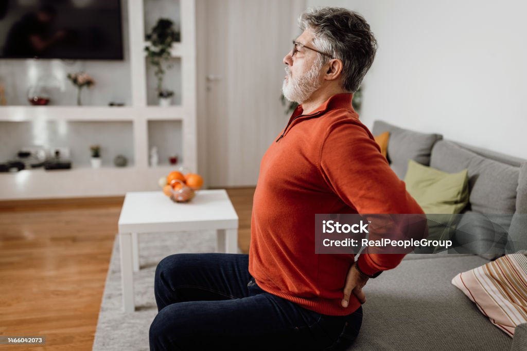 I should stretch more often Poor worried mature Caucasian man feeling strong pain in his back at home Backache Stock Photo