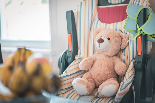 Toy soft bear siting in baby's Highchair at home kitchen