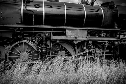 Steam train wheels driving in the countryside with smoke coming from the chimney. Black and white photograph.