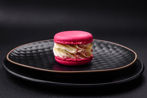 Beautiful tasty macaron with filling and fruit flavor on a black plate on a dark concrete background