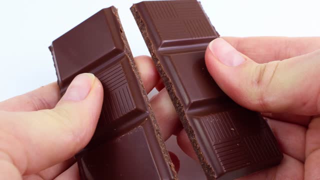Caucasian woman hands holding and breaking off chocolate from a bar close up