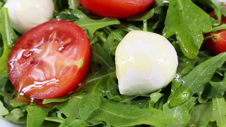 Green salad with arugula leaves, mozzarella balls and cherry tomatoes with olive oil pouring on it and circle rotation