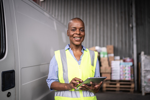 Portrait of a mature woman working on a digital tablet beside a delivery van