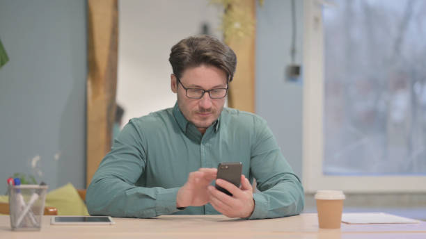istock Mature Adult Man Browsing Internet on Smartphone at Work 1466073818
