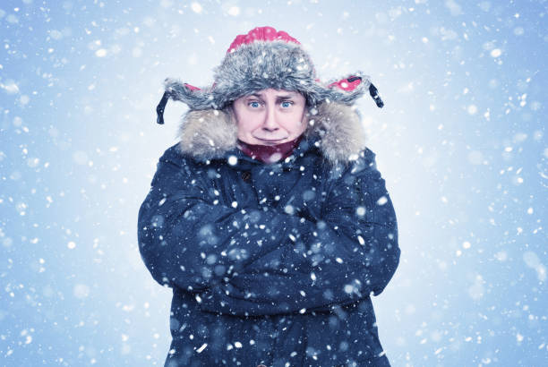 istock Frozen man in winter clothes warms his hands in his sleeves, on a light blue background with snow 1466077559