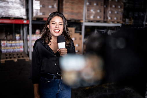 Reporter talking on a microphone in a warehouse