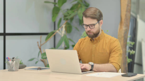 istock Beard Young Man Typing on Laptop in Office 1466088101