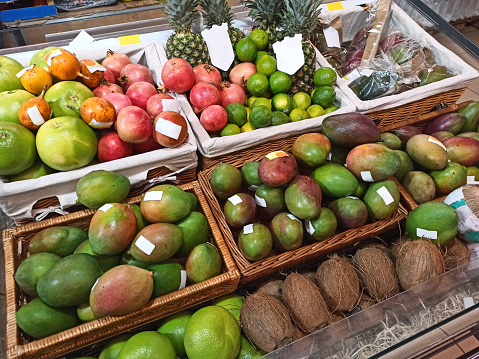 Top view: ripe fresh and organic exotic fruits, mango, coconut, pineapple, pomegranate, lime in wicker baskets for sale in a grocery supermarket. Healthy raw vegan food and healthy lifestyle concept