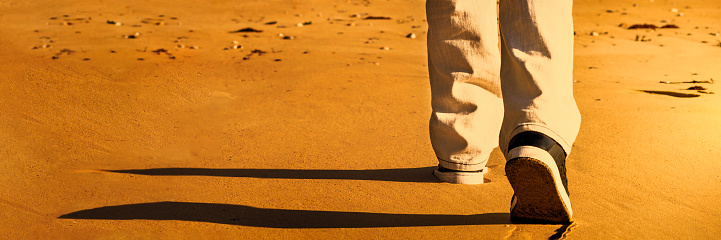 Man walking on the sand at sunset, seen from behind, photo