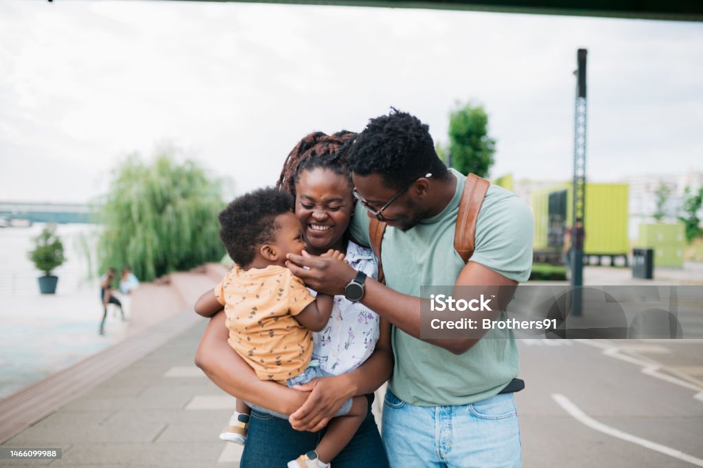 Happy african family having fun together outdoors Happy african family having fun together outdoors. Woman carrying her son with man pulling boy's cheek while walking outside in the city. Family Stock Photo