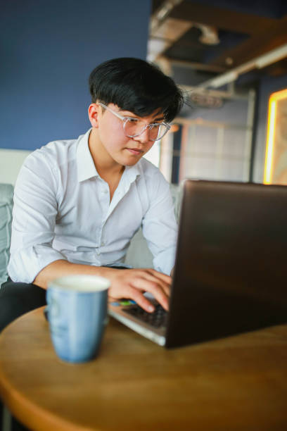 istock Young man with slanting eyes working hybrid remotely from laptop in cafe. 1466102940