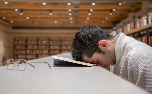istock a young man gets tired while reading a book in the library. 1466105203