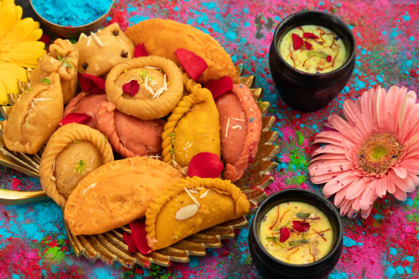 indian festival of colors holi is celebrated with colorful gulal abeer, kesar pista badam thandai, gujiya, mawa potli gujia, chandrakala, mithai, water gun, dry fruits, bhang, laung latta, samosa - toy gun imagens e fotografias de stock