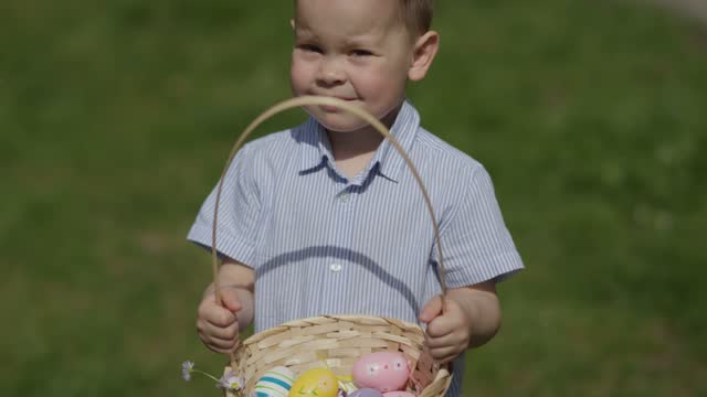 funny little boy kid holding Easter basket colorful eggs in hands posing front of camera sunny warm spring day