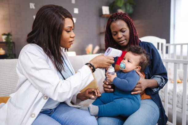 black female healthcare worker visiting mother and her son at home, examining him with contactless infrared thermometer checking for body temperature - infrared thermometer imagens e fotografias de stock