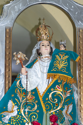 Image of the Virgin of Carmen with green dress and golden and other colored accessories on her altar surrounded by several flowers, located in Shupluy, Yungay, Ancash, Peru.