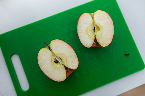 Photo of a red apple cut in half on a green board shot from above