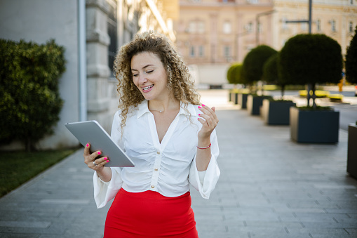 Portrait of a beautiful young woman enjoying coffee outdoors and using a digital tablet