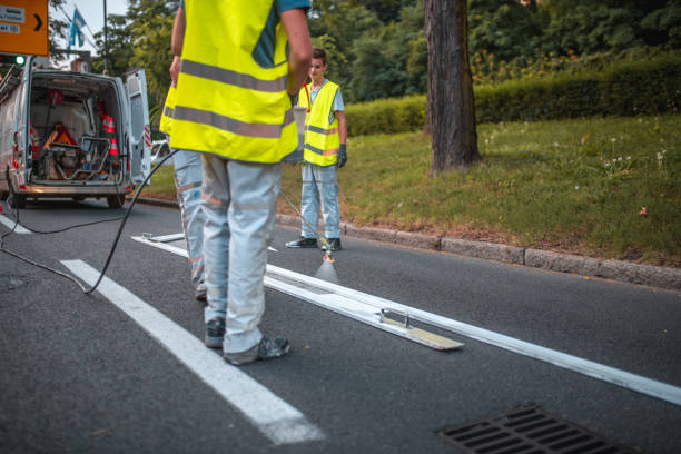 Road Maintenance Crew Spray Painting A Road Using A Stencil Road maintenance crew spray painting a road using a stencil. All wearing a reflective vest and one guy spraying the paint inside the stencil. freshly painted road markings stock pictures, royalty-free photos & images