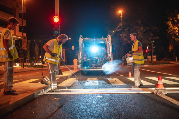 Road Maintenance Workers Spray Painting  A Crosswalk With A Spray Gun Road maintenance workers wearing a reflective vest spray painting a new layer of white paint on a crosswalk using a spray gun. freshly painted road markings stock pictures, royalty-free photos & images