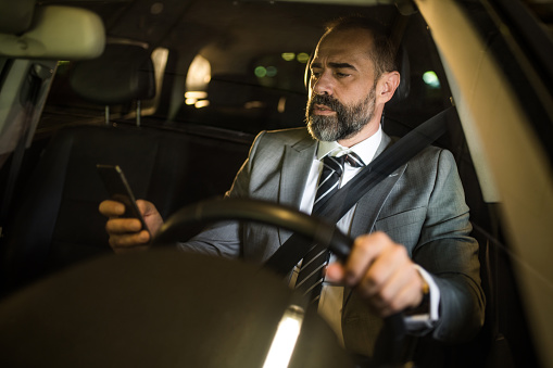 Mid adult businessman in his late 40's driving his car and using phone.