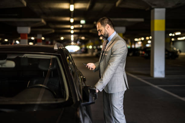 istock Mid aged man using phone while standing next to his car in public garage. 1466156269
