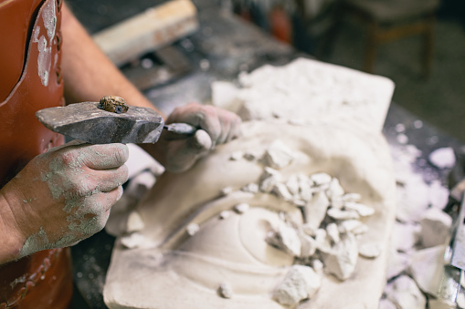 Man sculptor creates sculpt bust gypsum human woman sculpture with hammer. Statue craft creation workshop.