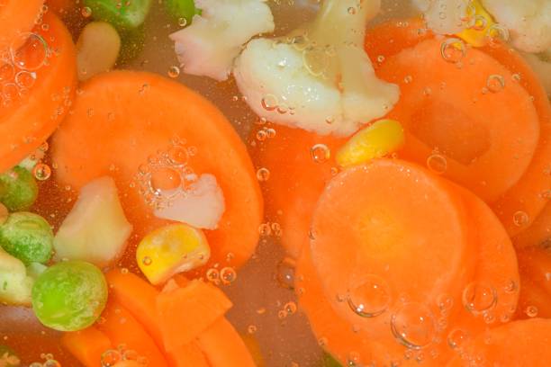 istock Close-up fresh soup vegetables with carrots, peas, cauliflower and corn on white background. Soup vegetables with carrots, peas, cauliflower and corn in boiling water on white background, close-up. Horizontal image. Top view, flat design 1466171871