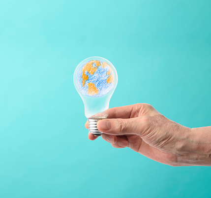 Close-up of hand holding a light bulb with the Earth in it against light blue background.
Climate Change.
Alternative energy concept.