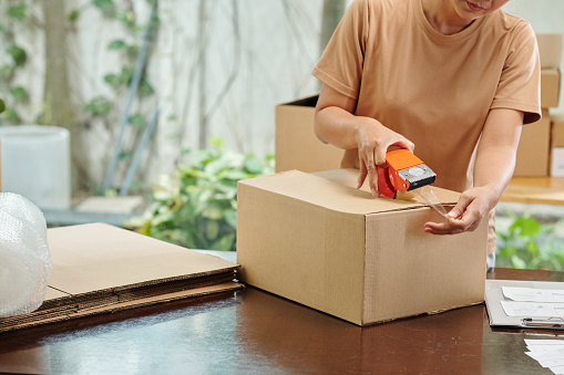 Woman packing orders and sealing cardboard boxes for delivering to clients