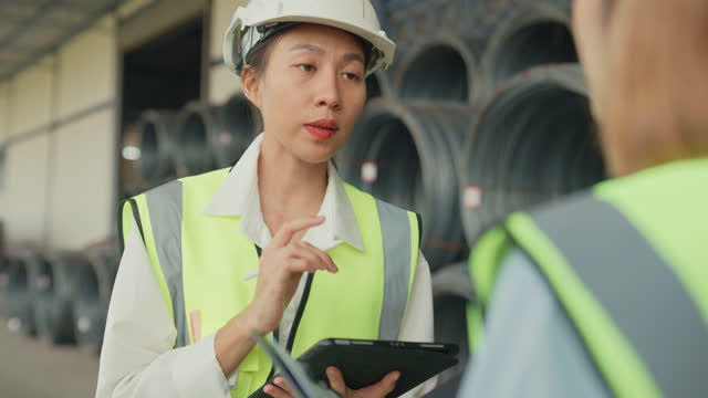 Close up of young Asian female industrial engineer in hard hats discuss new project in wire manufacturing factory. Heavy Industry and engineers team.