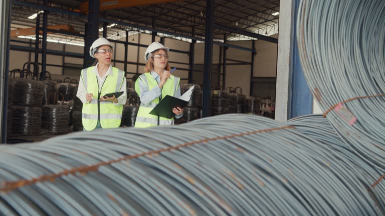 Young Asian female industrial engineer in hard hats discuss new project in wire manufacturing factory. Heavy Industry and engineers team.