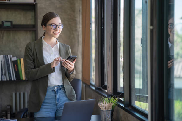 istock A happy young woman talking on her mobile phone and smiling while standing at her working place in the office. 1466197075