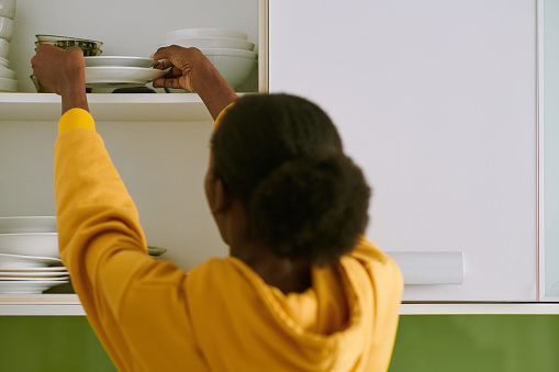 Woman putting clean plates in kitchen cabinet