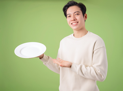 Image of young Asian man holding plate on background