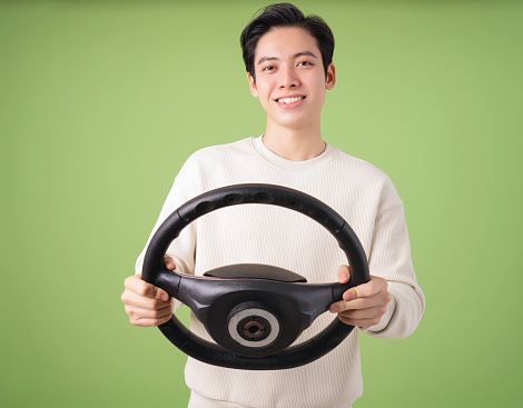 Image of young Asian man holding steering wheel on background