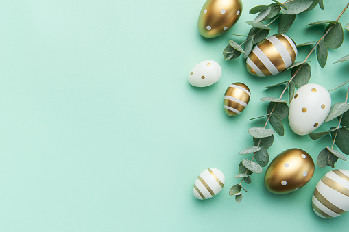 Easter eggs painted in gold and eucalyptus branches on a soft green background. Festive background