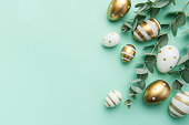 Easter eggs painted in gold and eucalyptus branches on a soft green background.