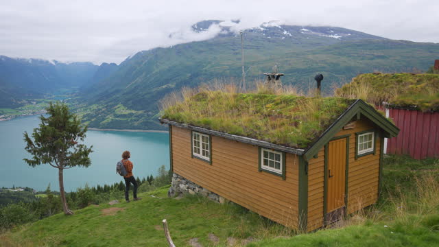 Man with backpack standing near the hut with moss on roof in Norway