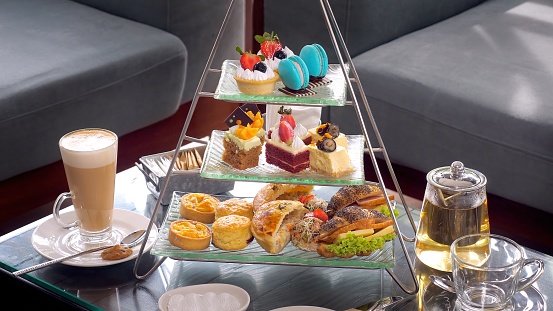 Colorful afternoon tea table with glass teapot, fresh fruit cakes, and an array of delicious desserts, sandwiches and pastries with hot coffee in luxury restaurant. Delicious sweet food.