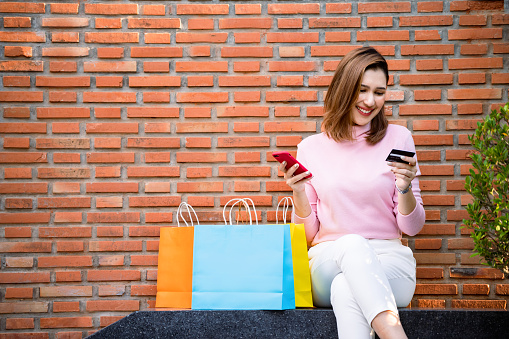 Young fashion woman shopping online with smartphone and credit card with colorful shopping bags next to it.