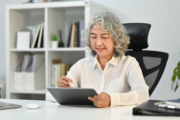 istock Beautiful middle aged woman using digital tablet while remote working from home. 1466261624