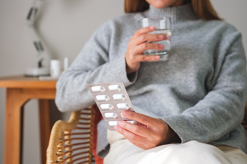 Closeup image of a woman holding pills blister pack and a glass of water